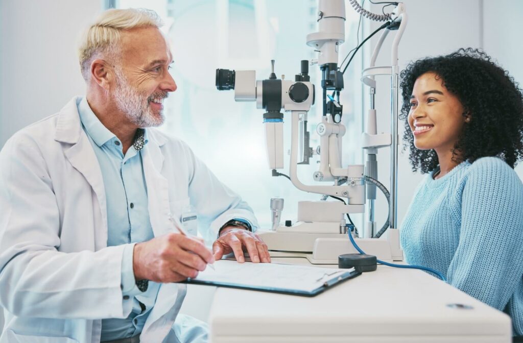 An optometrist and a patient smiling during an eye exam while discussing her Medicaid coverage.