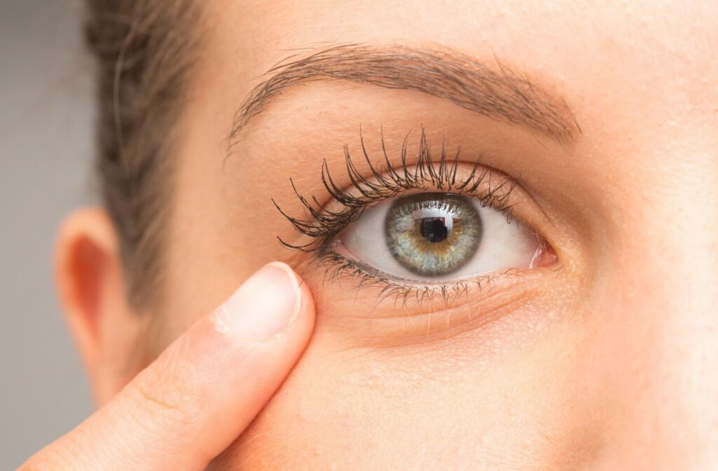 Close-up of a person pointing to their lower eyelid, showing a clear green eye and surrounding skin.